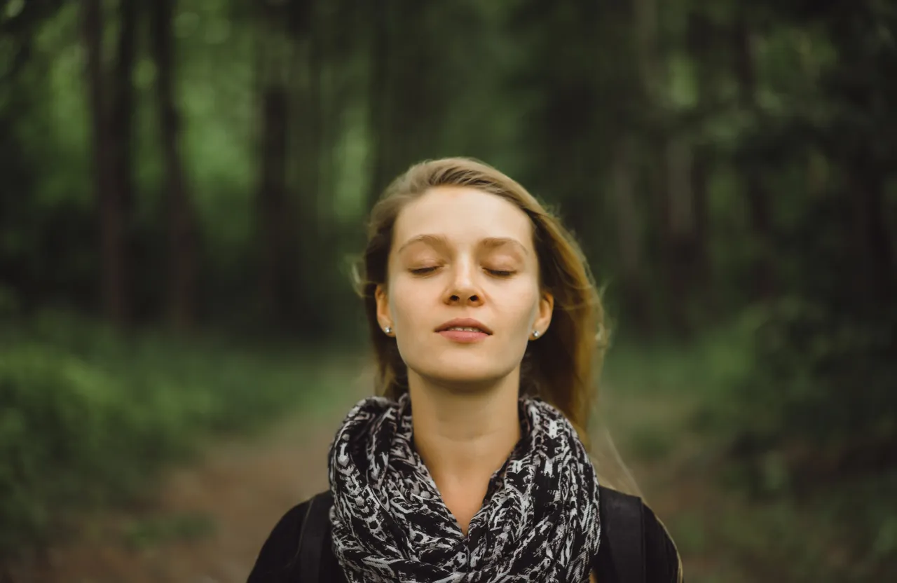 a woman with her eyes closed standing in a forest