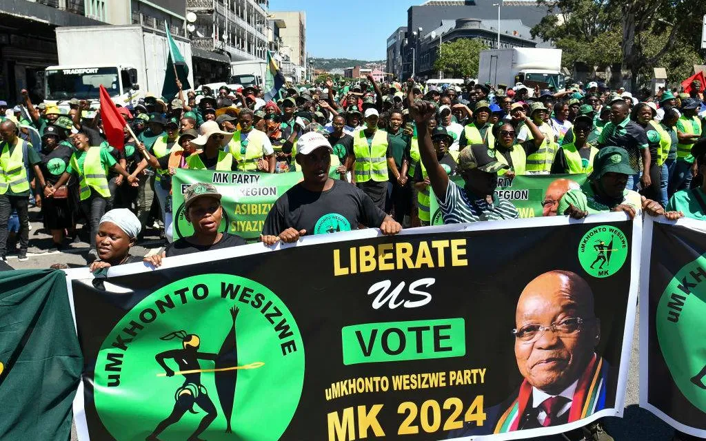 a large group of people holding campaign signs and flags written vote MK party 2024