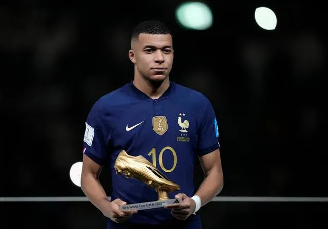 Kylian mbappe holding a golden boot in his hands