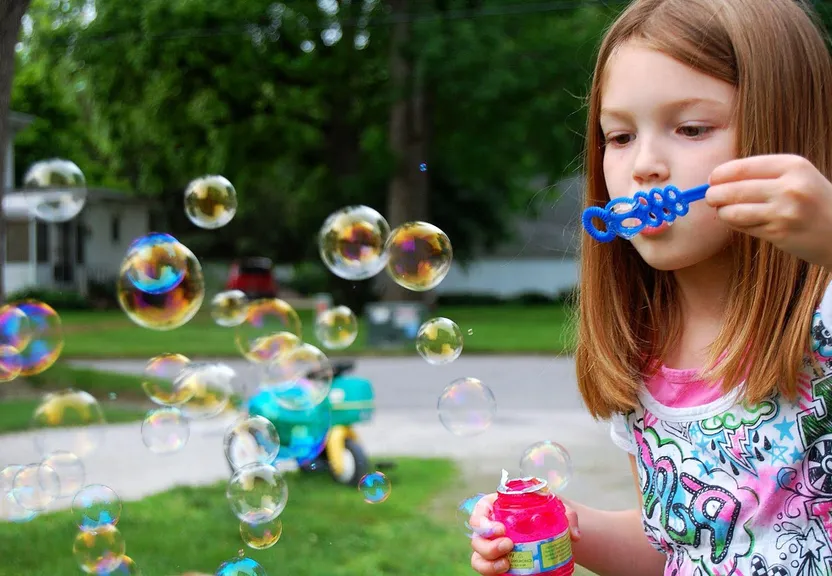 a little girl blowing bubbles on a lawn