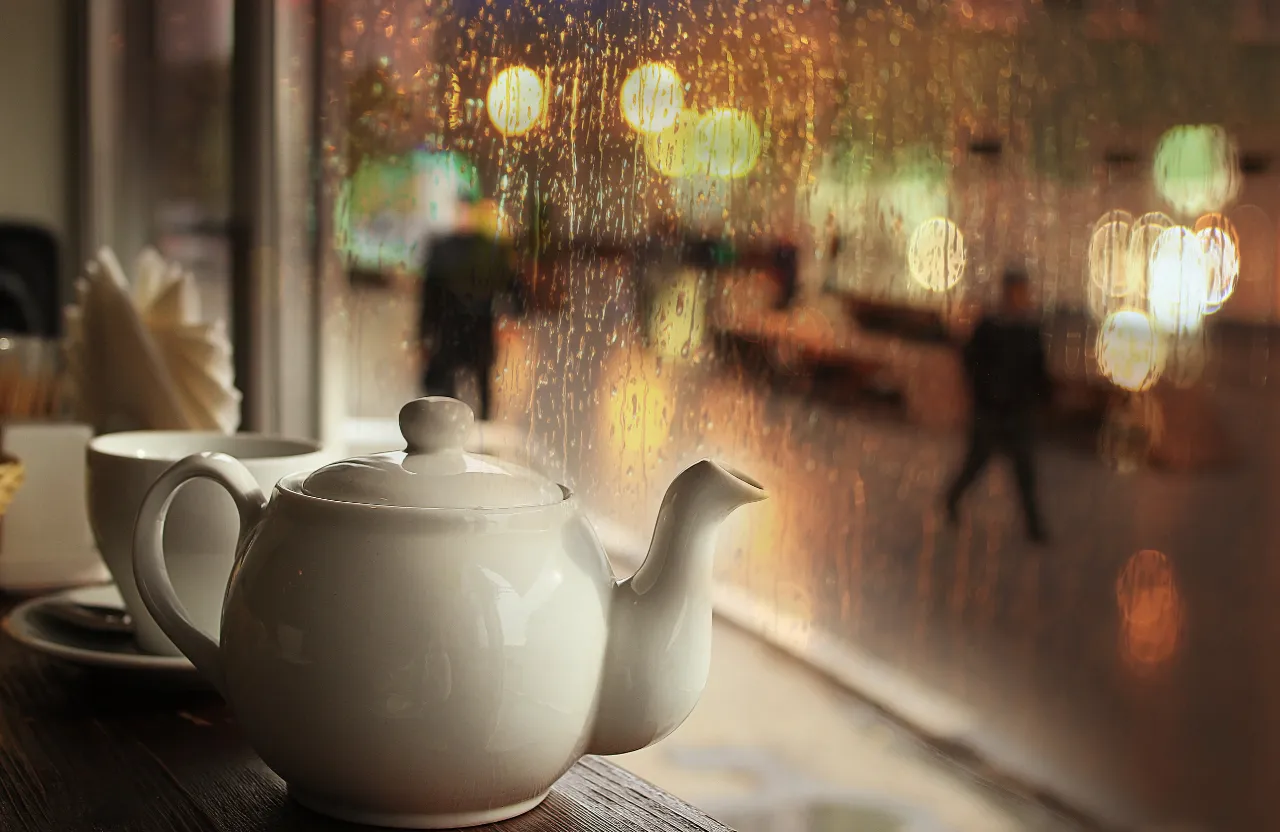 A white teapot on a clean wooden table, with a single flower in a vase, bamboo mat and a backdrop of a serene koi pond