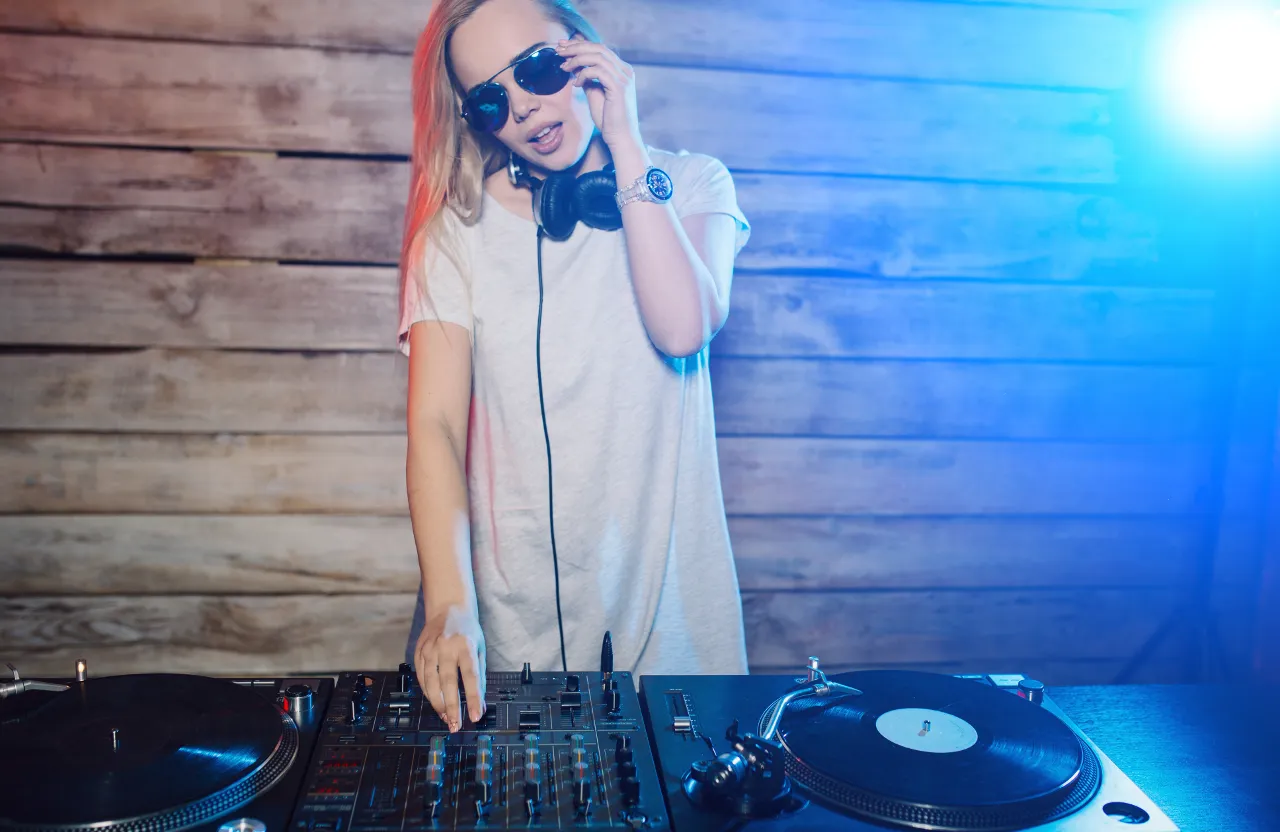 A woman in sunglasses and headphones is using a dj's turntable