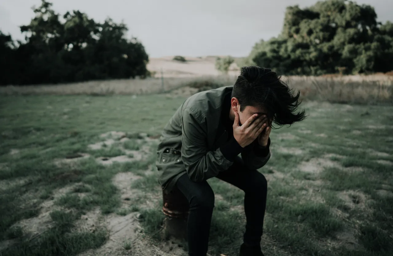 a man kneeling down in a field with his head in his hands and crying