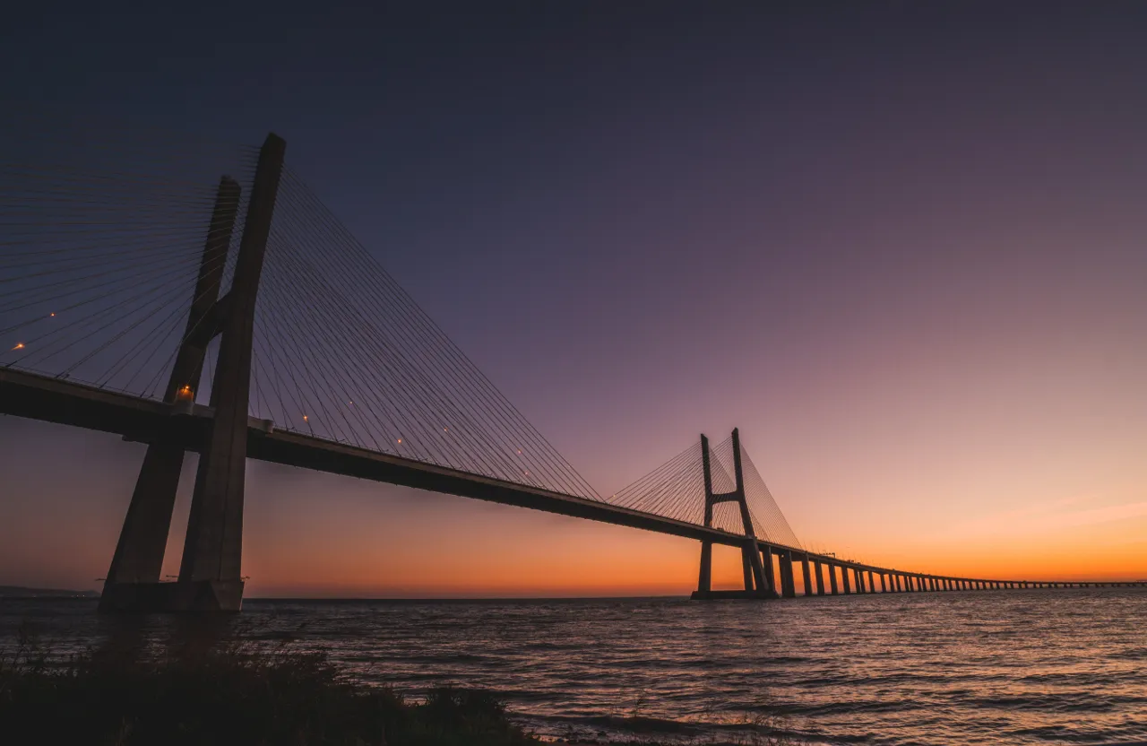 the sun is setting behind a bridge over the water