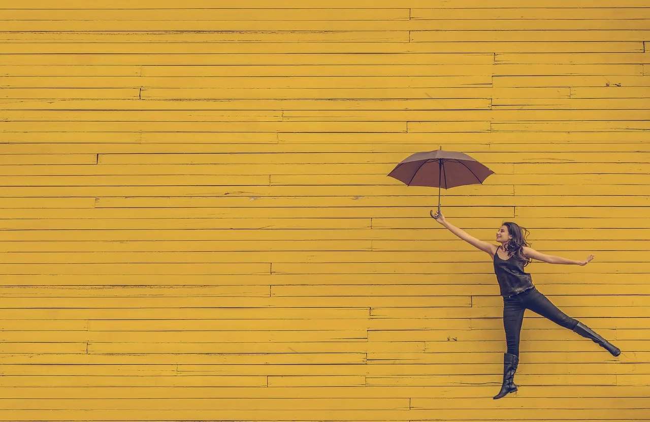 a woman holding one umbrella in front of a yellow wall