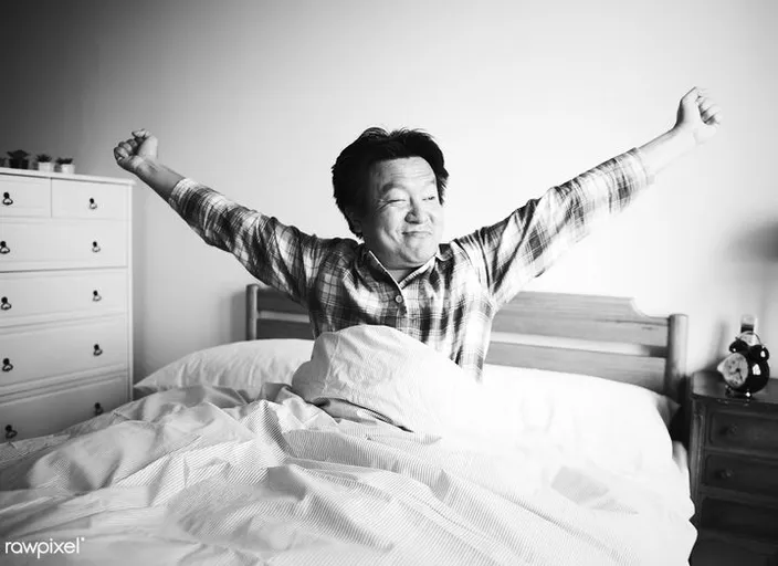 a man awakening from deep sleep ,sitting on top of a bed with his arms in the air