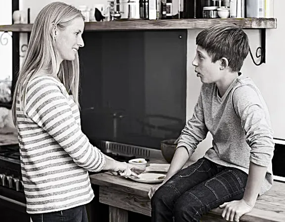 a woman sitting on a counter talking to a boy