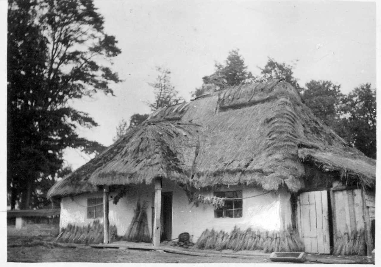 a black and white photo of a house with a thatched roof