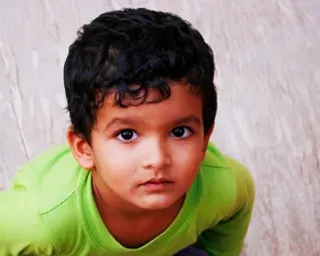 a young boy in a green shirt sitting on the ground