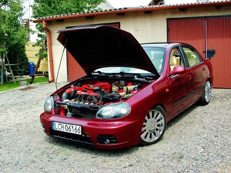 a red car with its hood open on a gravel driveway