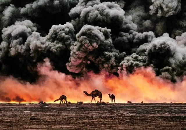 a group of camels standing in front of a large plume of smoke