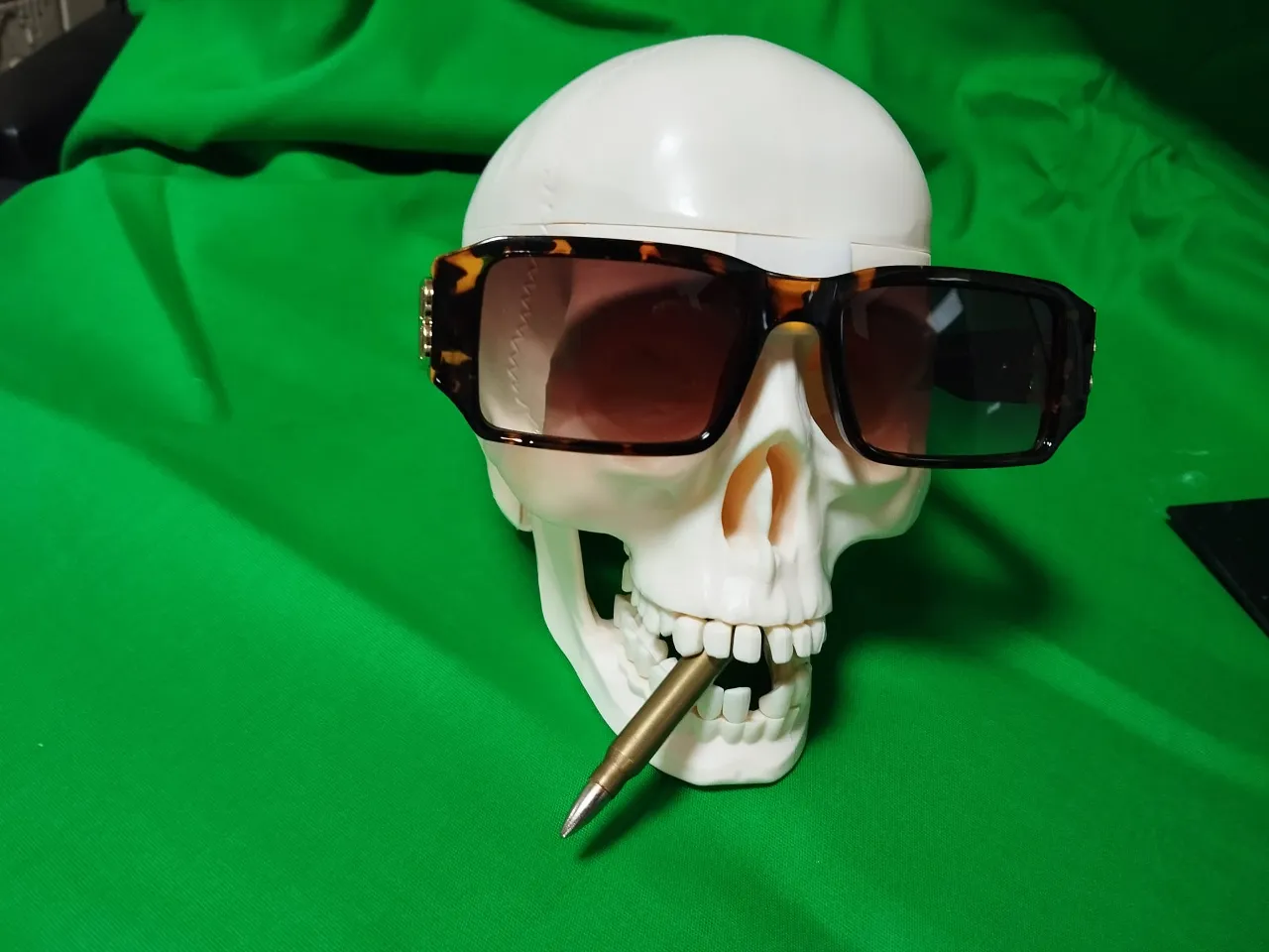 a fake skull with sunglasses and a pen sticking out of it's mouth