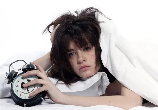 a woman laying in bed with an alarm clock