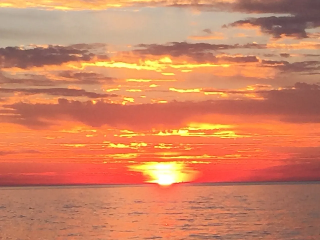 the sun is setting over the ocean on a cloudy day