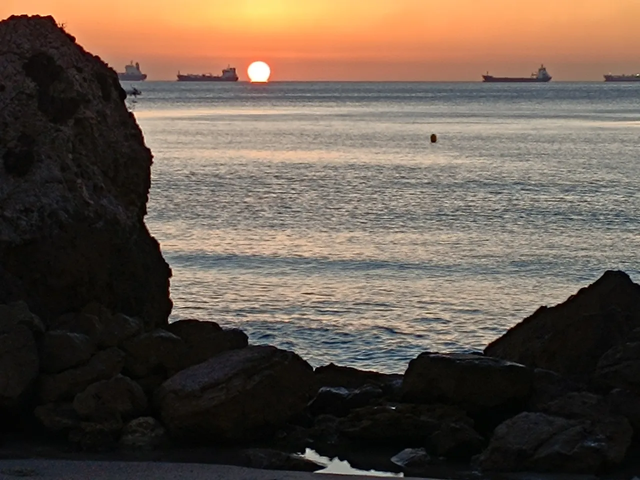 the sun is setting over the ocean with ships in the distance