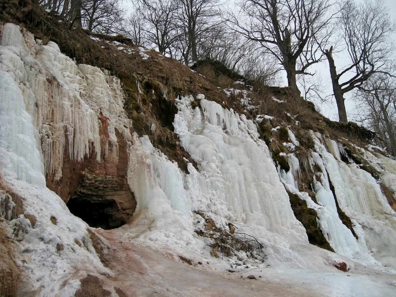 a very tall waterfall covered in ice next to a forest