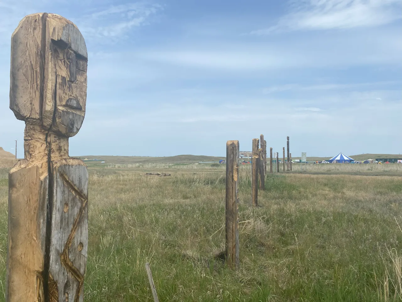 a wooden sculpture in a grassy field with a tent in the background