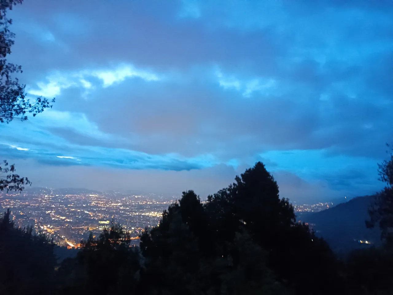 a view of the city lights from the top of a hill