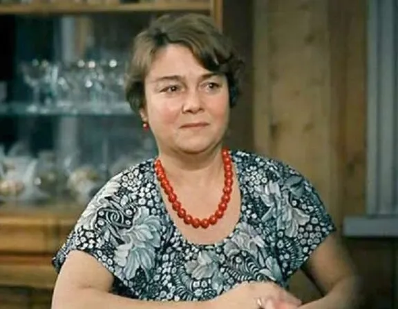 a woman sitting at a table with a red beaded necklac