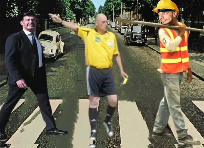 A young man, wearing a yellow worker's helmet, receives a yellow card from a soccer referee at a pedestrian crossing. Meanwhile, a laughing, overweight executive approaches. Neither of them wears glasses.

