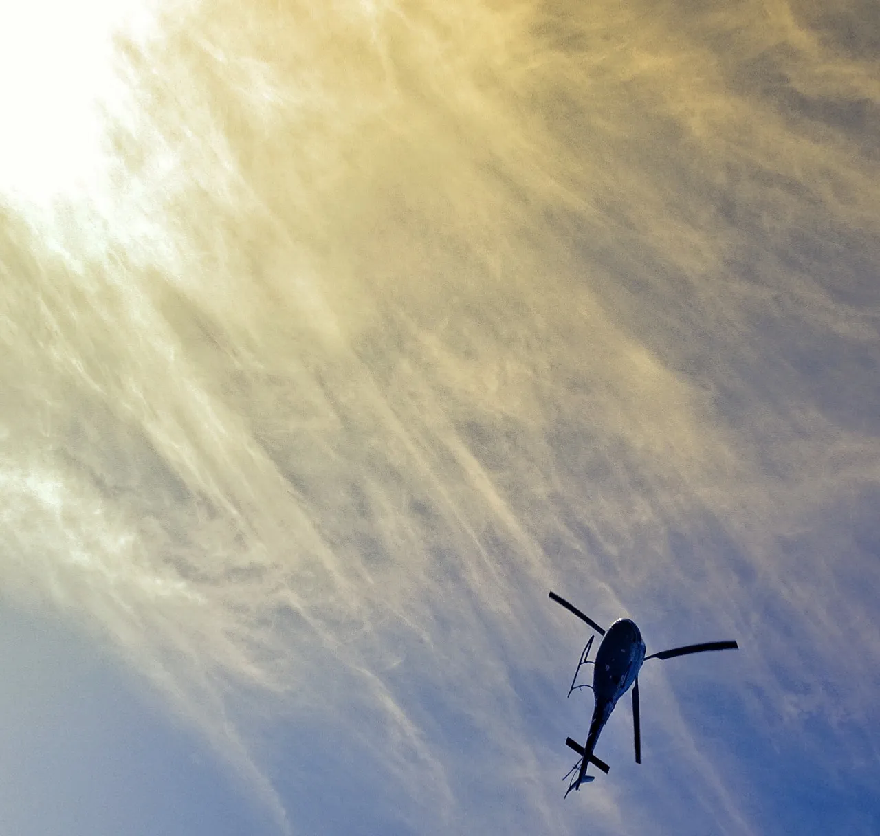 a helicopter flying through a cloudy blue sky