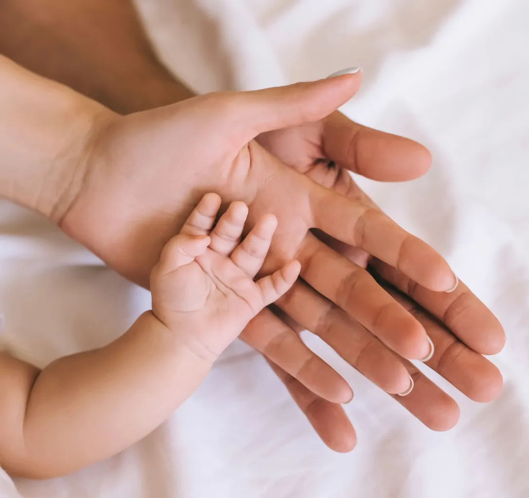 a woman holding a baby's hand on top of a bed