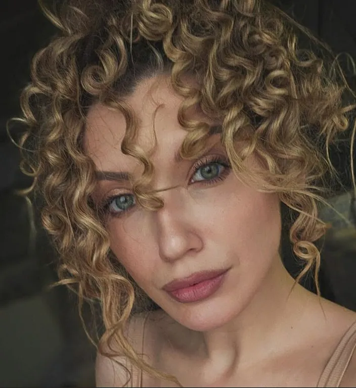 Close up of a woman with curly hair, raindrops running down her glowing face and tangled locks