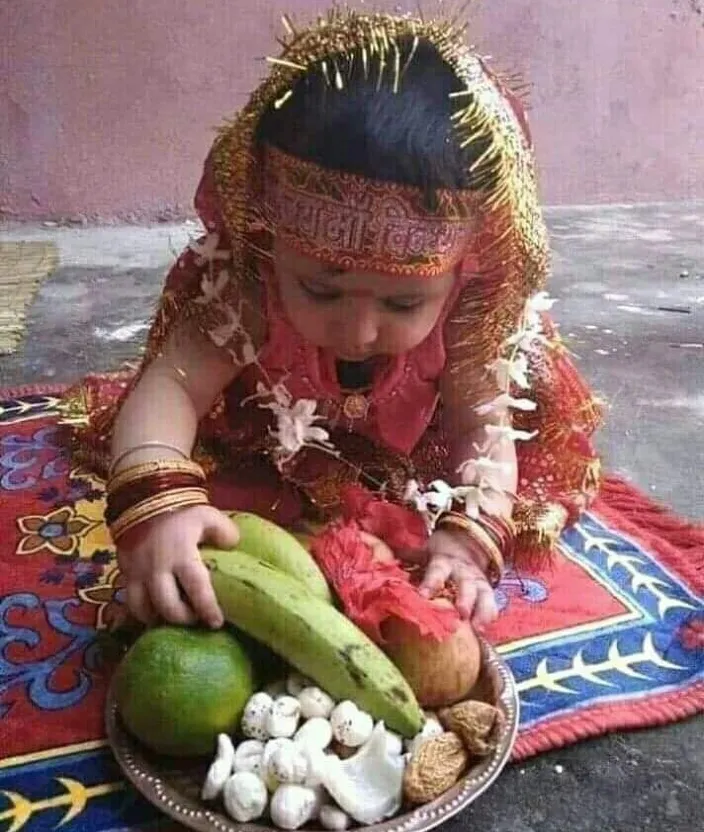 a little girl in a headdress sitting on a rug with a plate of