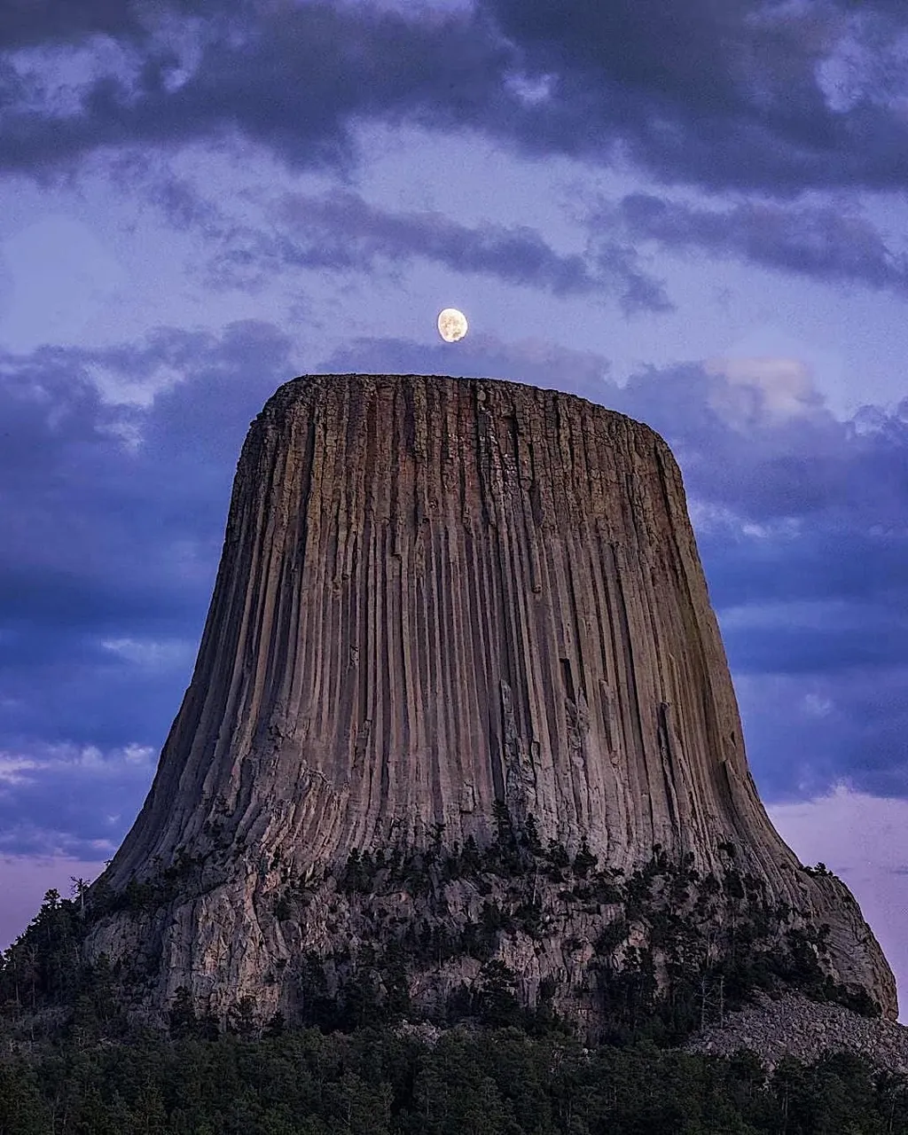 a full moon rises over a tall rock formation