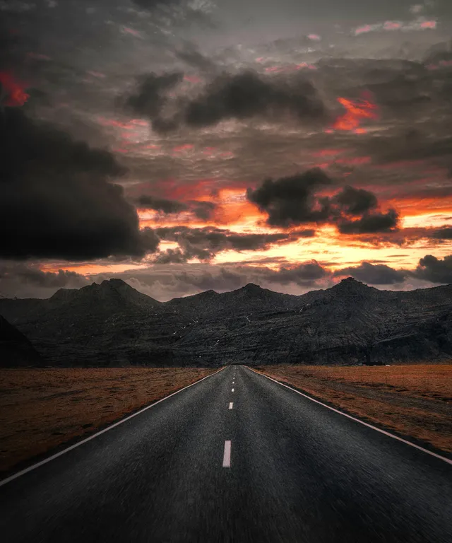 a long empty road with mountains in the background