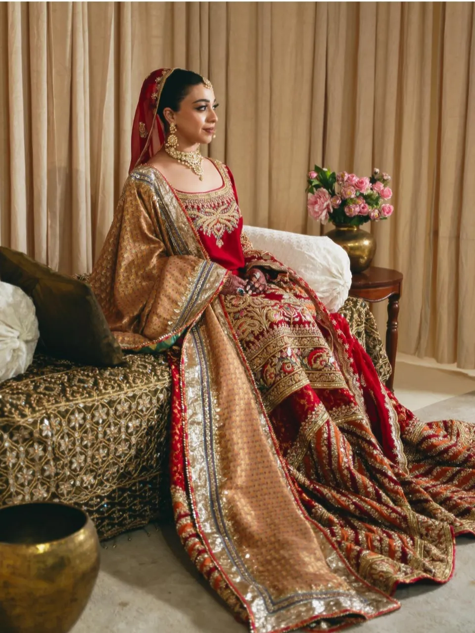 A woman in a red and gold dress sitting on a plush couch, bathed in golden hour light