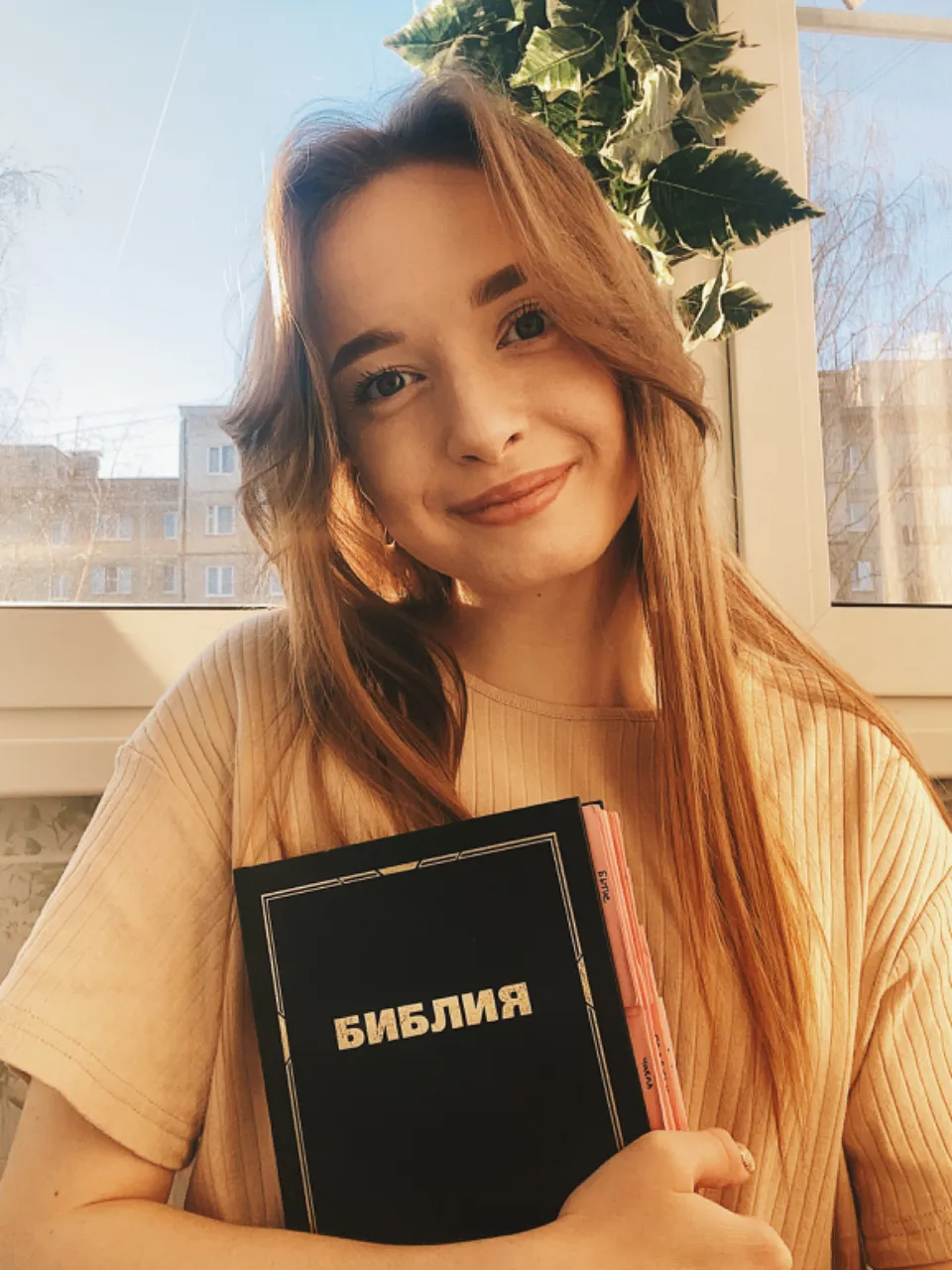 a woman holding a book in front of a window