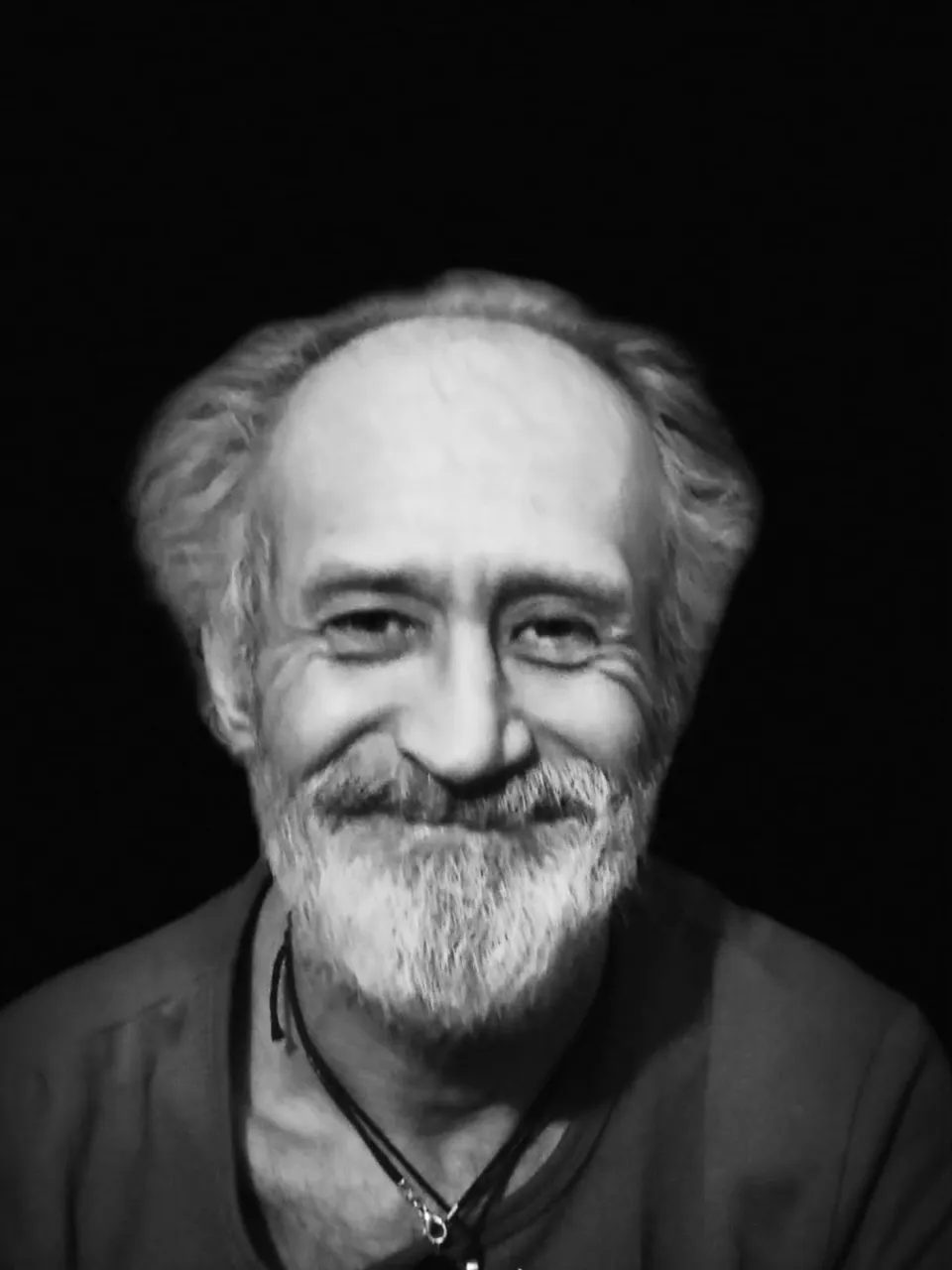 A black and white portrait of a man with a beard staring at the moon on a clear, starry night