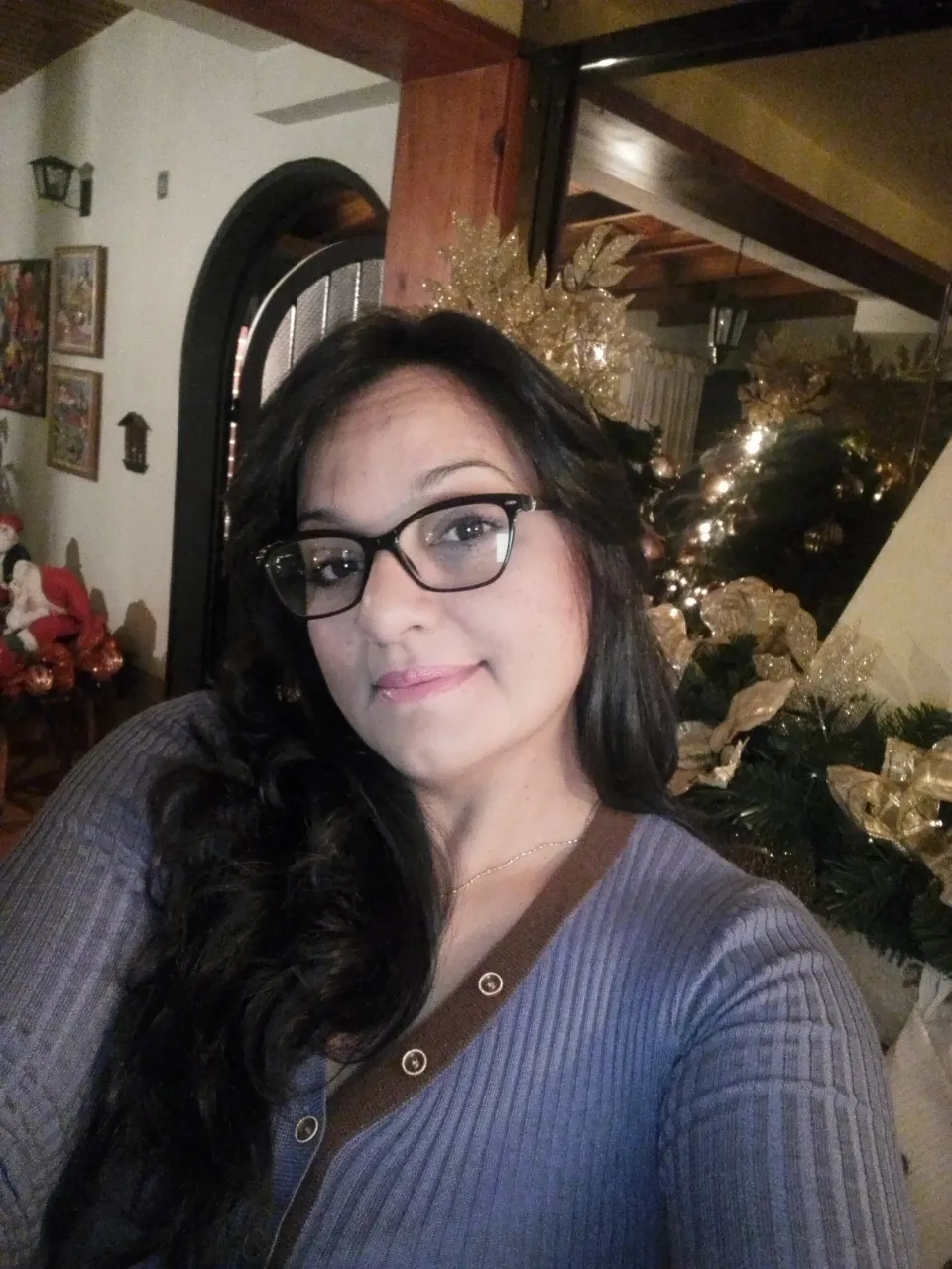 a woman wearing glasses standing in front of a christmas tree