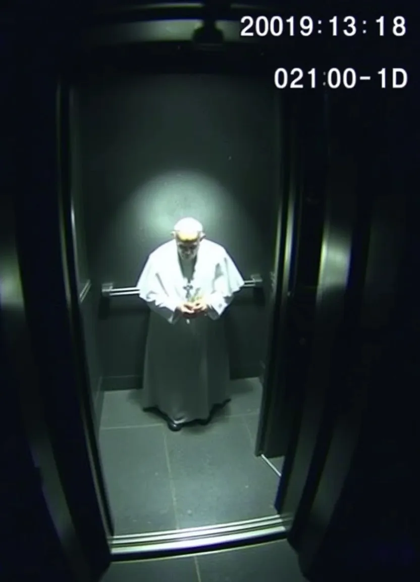 A realistic security camera footage image showing a dimly lit elevator with the pope trapped inside. The scene is captured from a high perspective, typical of a security camera. The image is slightly grainy with low resolution, simulating the look of real CCTV footage. The pope is standing alone in the elevator, The timestamp and camera ID overlay are visible in the top right corner of the screen, displaying the current date and time in white text. Shadows and dark areas dominate the scene, with a slight distortion or blur in the corners, typical of security footage lenses."