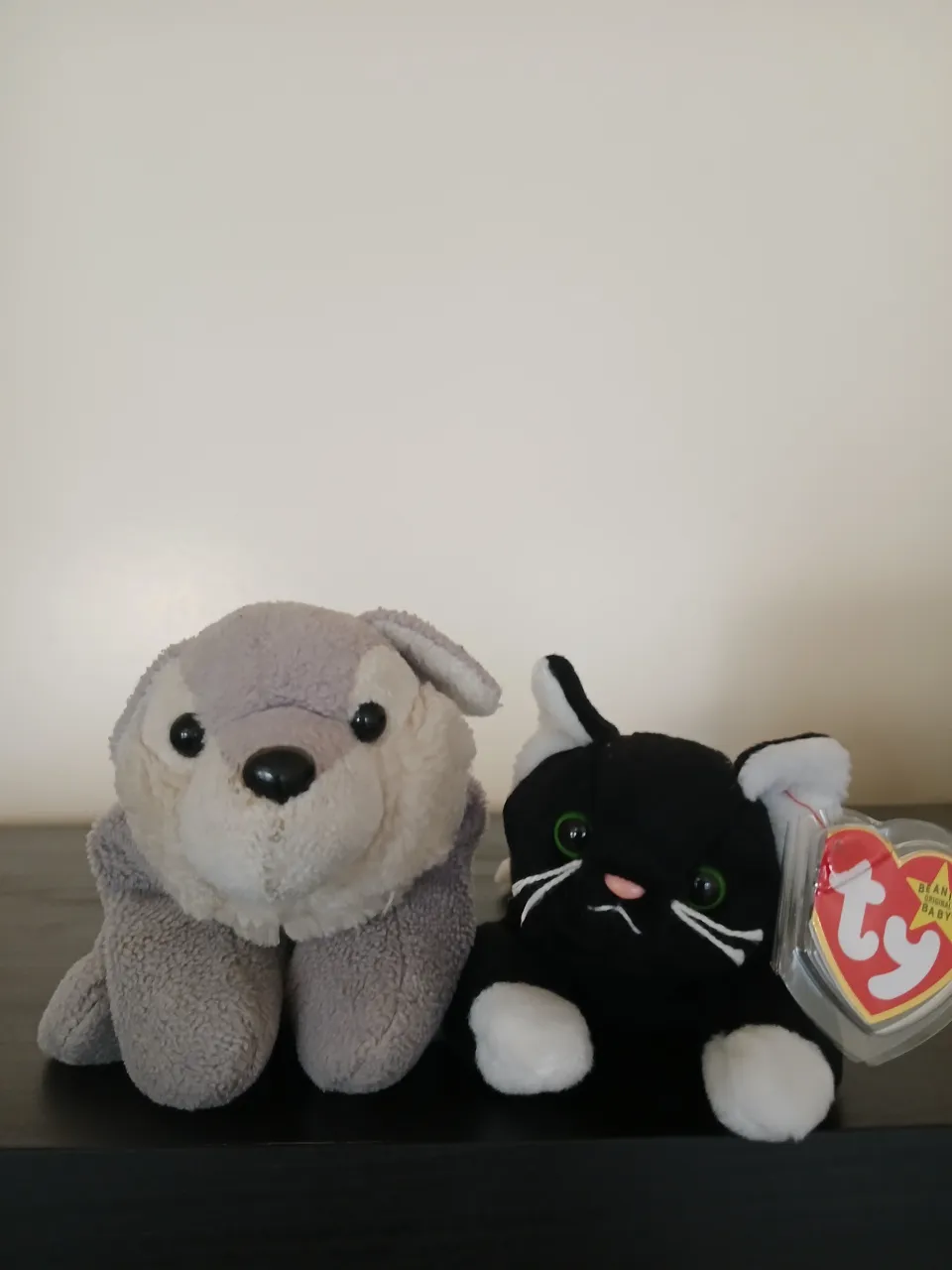 two stuffed animals are sitting on a table one is a grey wolf the other is a tuxedo cat