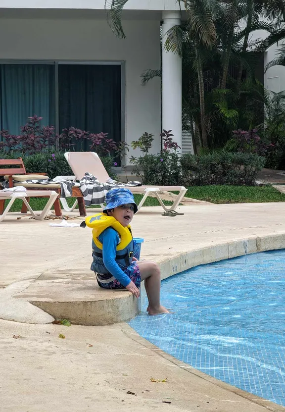 a young boy sitting on the edge of a swimming pool