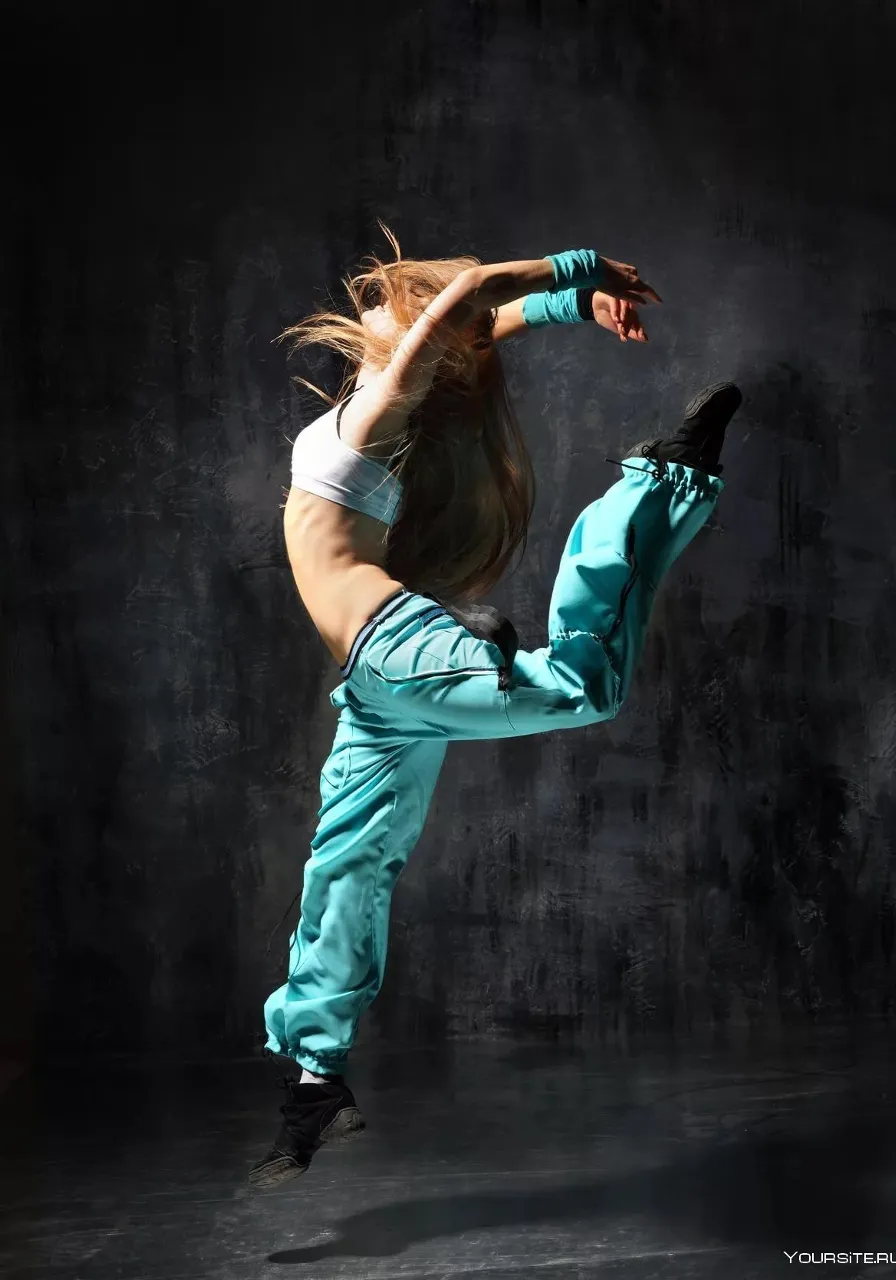 A woman in white shirt and blue pants doing a dance move under the neon lights of a city street.