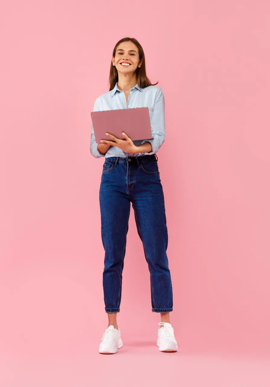 a woman in a blue shirt and jeans holding a laptop and is celebrating