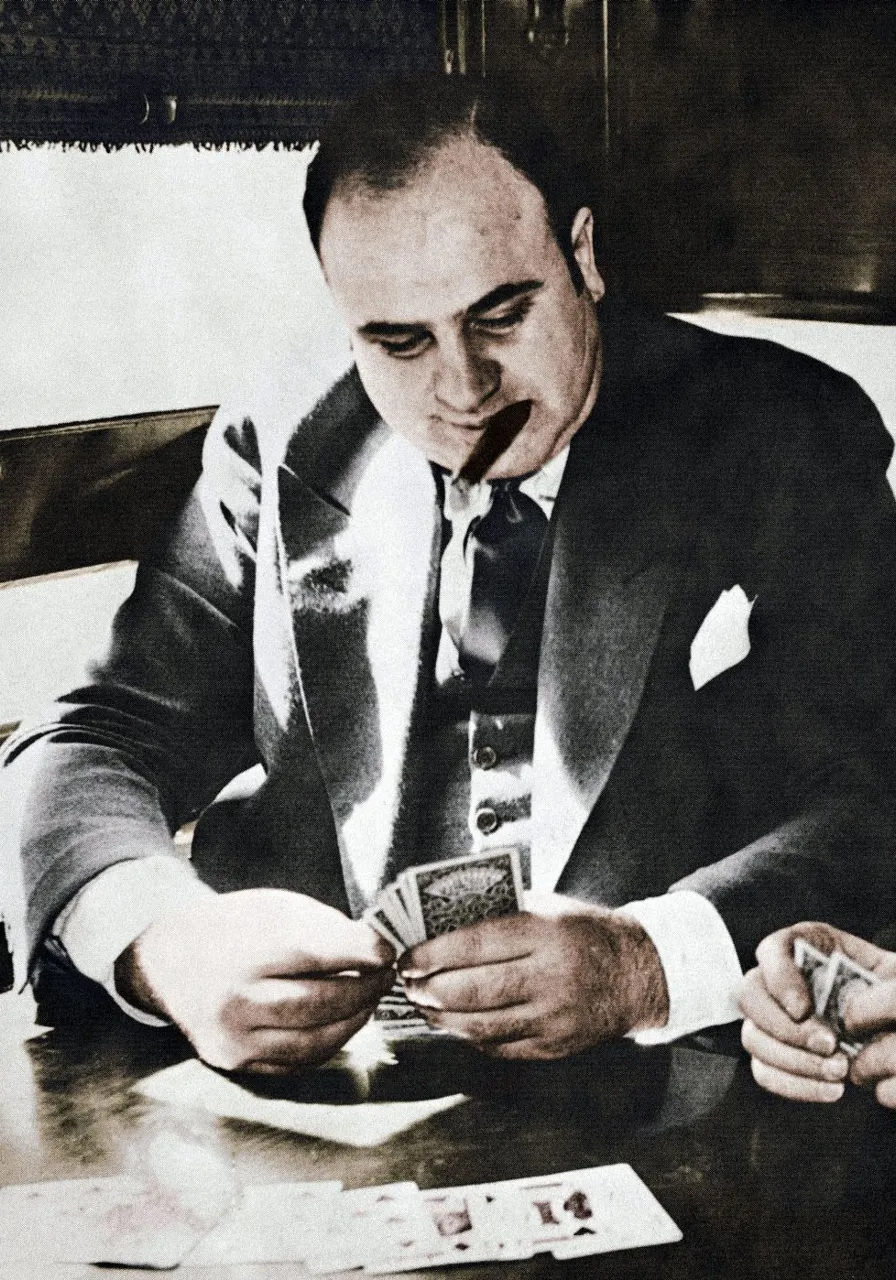 Аль капоне,a black and white photo of a man in a suit playing cards