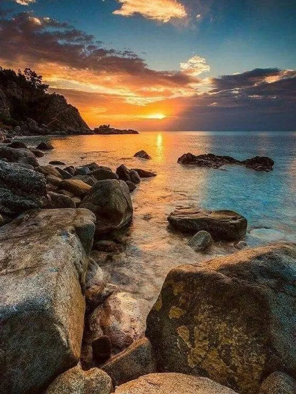 the sun is setting over a rocky beach