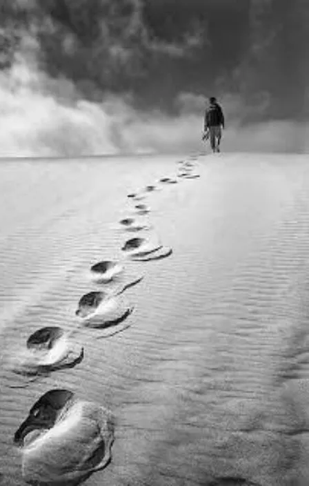 a man walking across a sandy beach under a cloudy sky