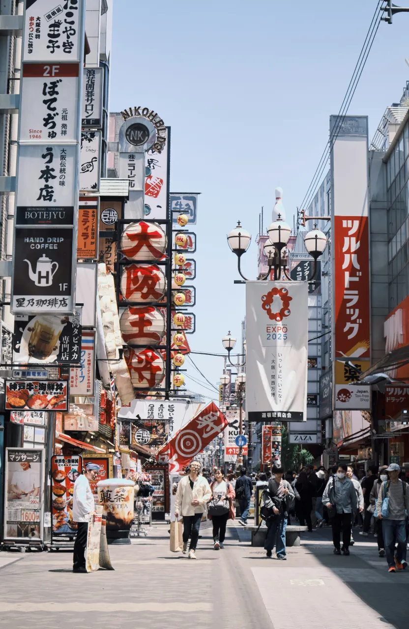 a group of people walking down a street next to tall buildings in Oasaka Japan