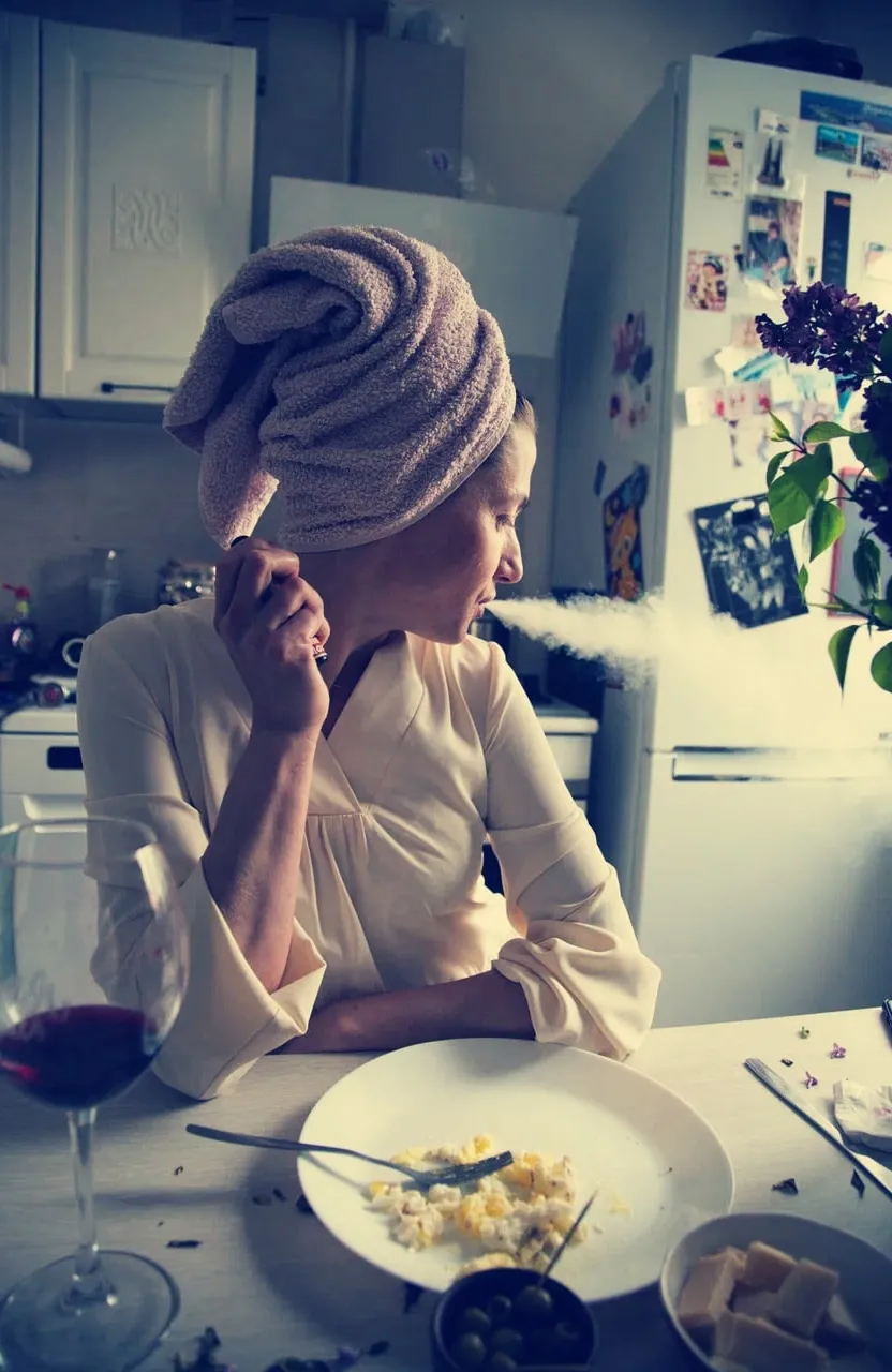 a woman sitting at a table with a plate of food, another glass of wine