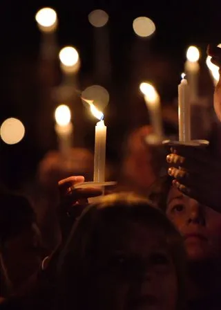 gathering of multiple people, holding candles aloft in the darkness.