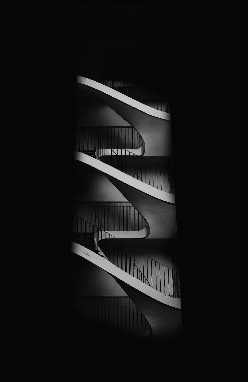 A minimalist black and white photo of a spiral staircase, casting a dramatic shadow