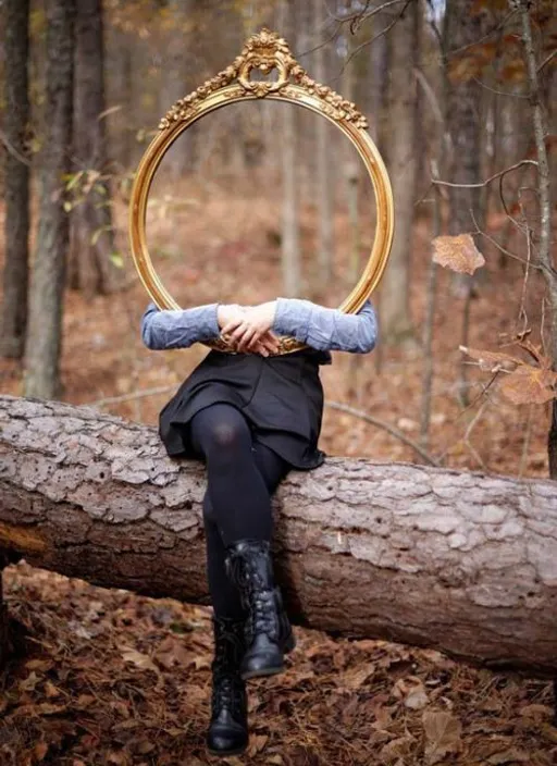 woman sitting on a tree trunk in the middle of the forest holding an oval mirror that covers her face