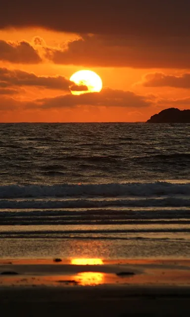 a sunset over the ocean with a small island in the distance