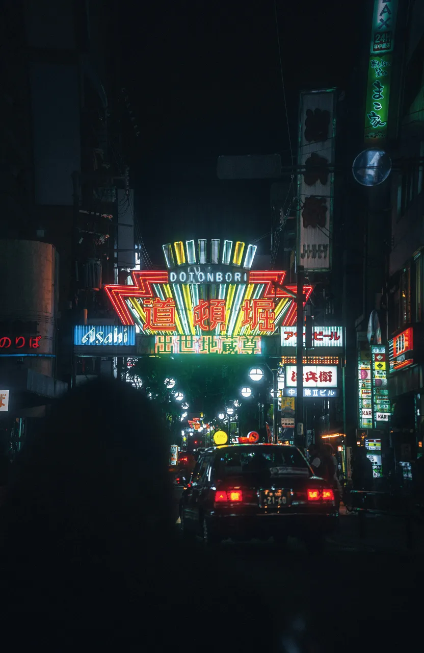 a busy city street at night with neon signs in Osaka Japan