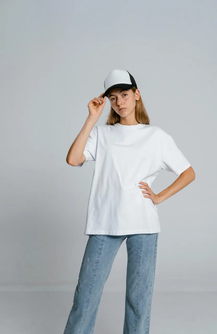 3D cartoon character wears jeans and a cap, posing with hand in hair, for a fashion shoot using stylized flash photography.